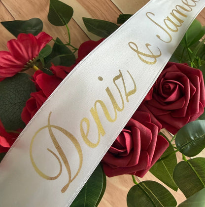 White sash with gold text 'Deniz' on a background of red flowers and green leaves.