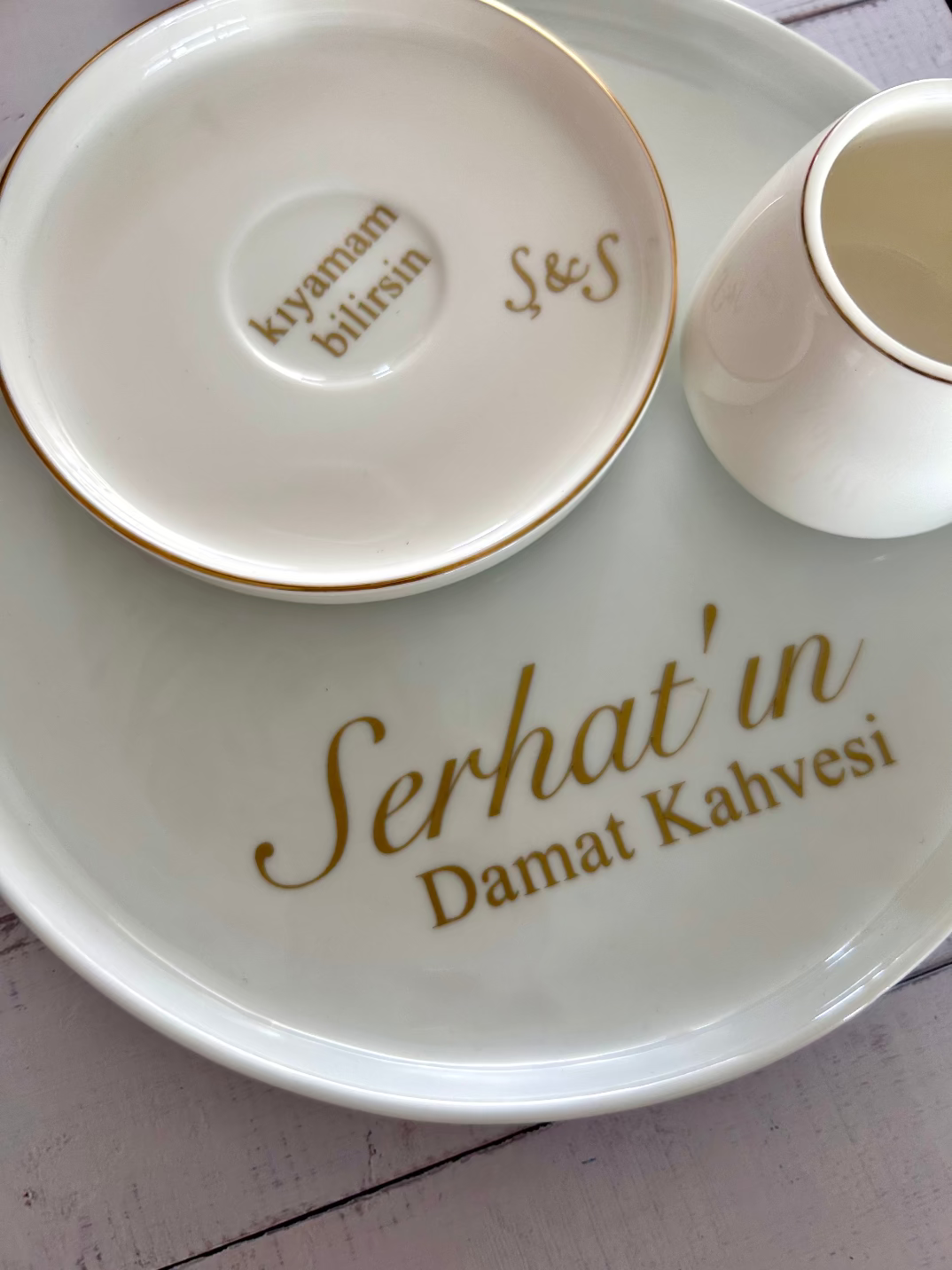 White ceramic plate with 'Serhat'in Damat Kahvesi' text, accompanied by a small cup and saucer.