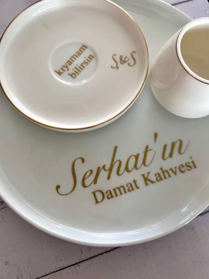 White ceramic plate with 'Serhat'in Damat Kahvesi' text, accompanied by a small cup and saucer.