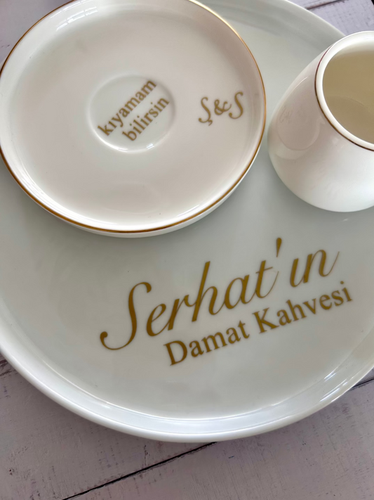 White ceramic plate with 'Serhat'in Damat Kahvesi' text, accompanied by a small cup and saucer.