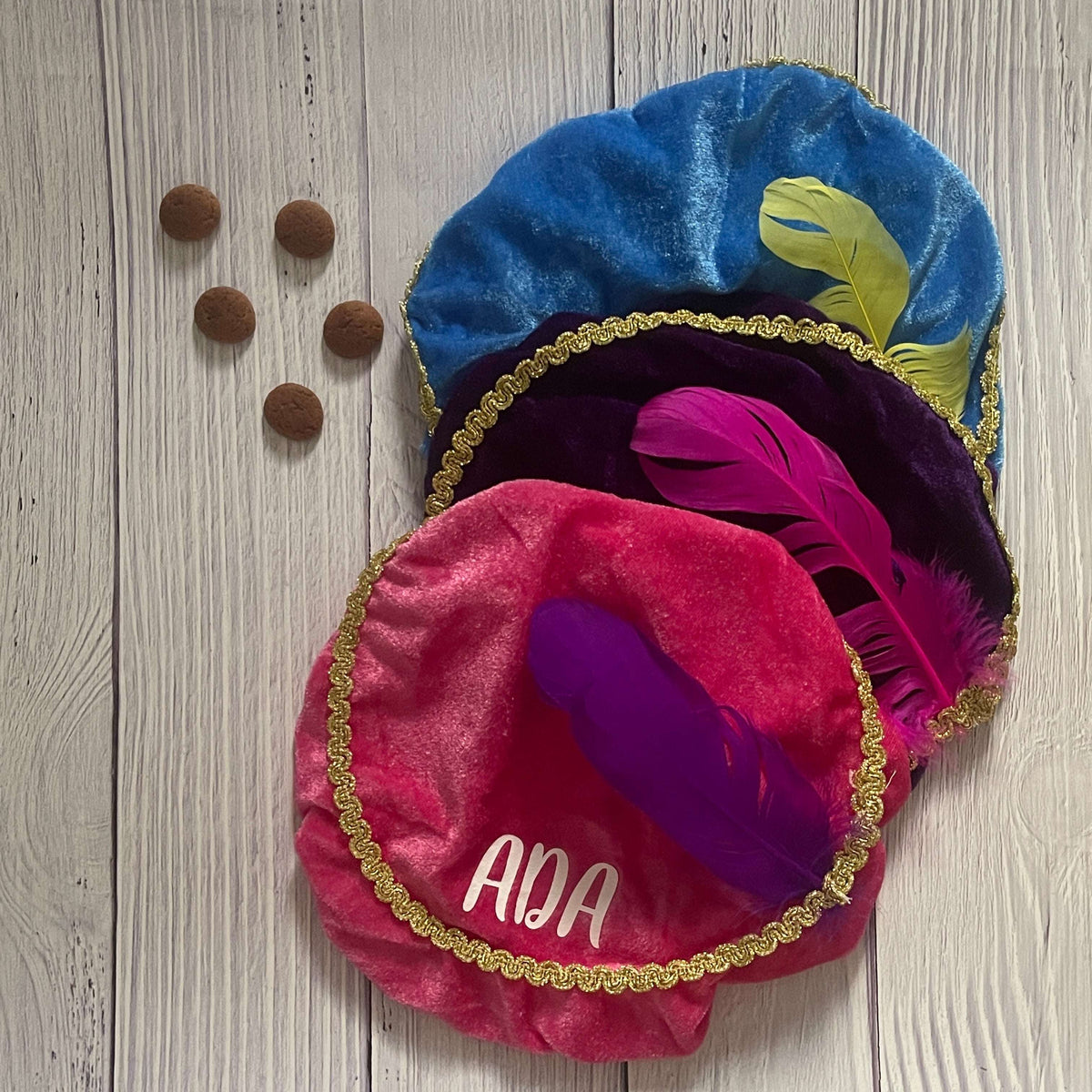 Gepersonaliseerde Piet hoed met naam in het rood met een veer op een houten achtergrond