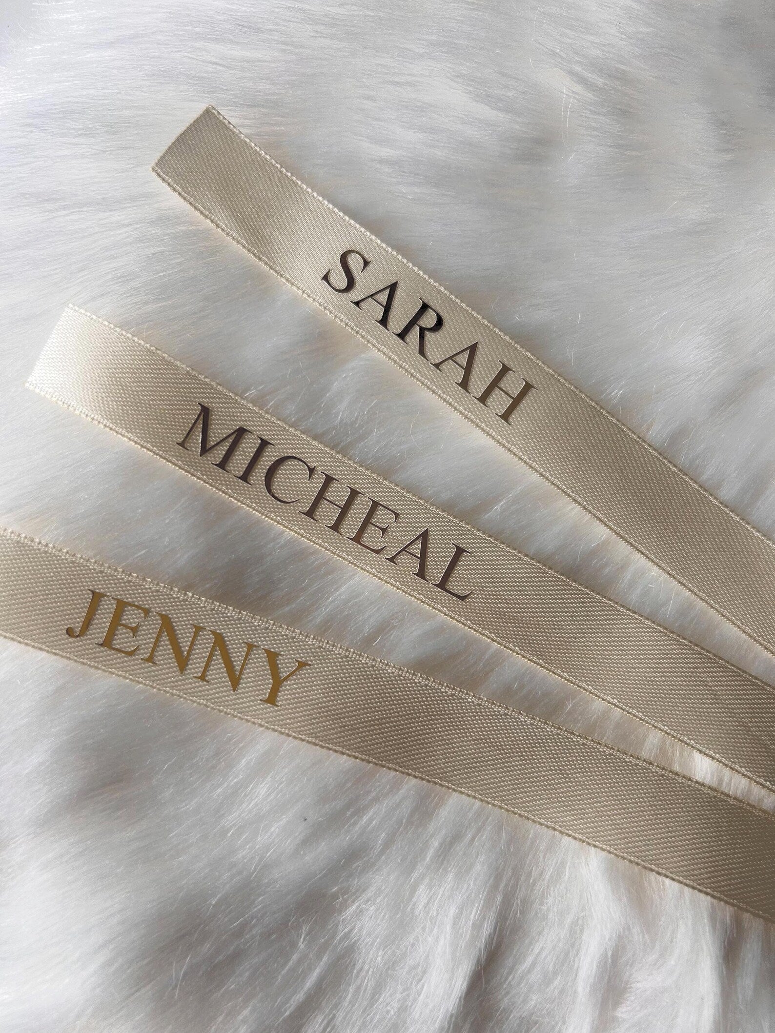Three cream ribbons with embroidered names on a white fur background