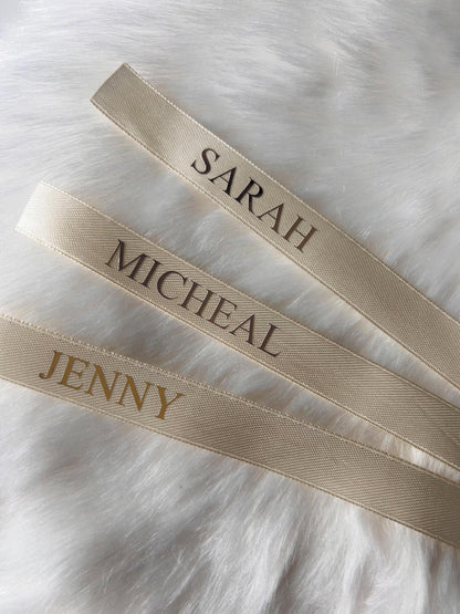 Three cream ribbons with embroidered names on a white fur background