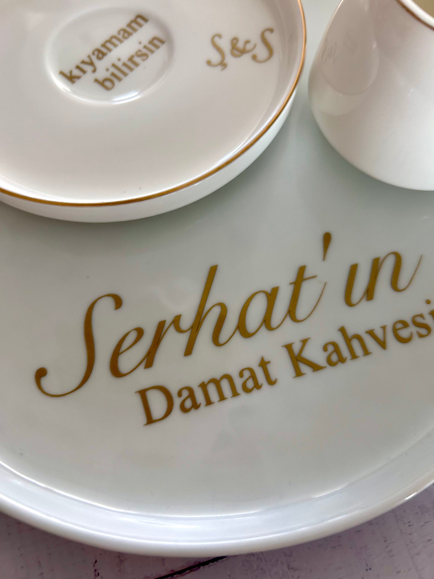 White ceramic plate with gold text 'Serhat'in Damat Kahvesi' and a small dish in the background.