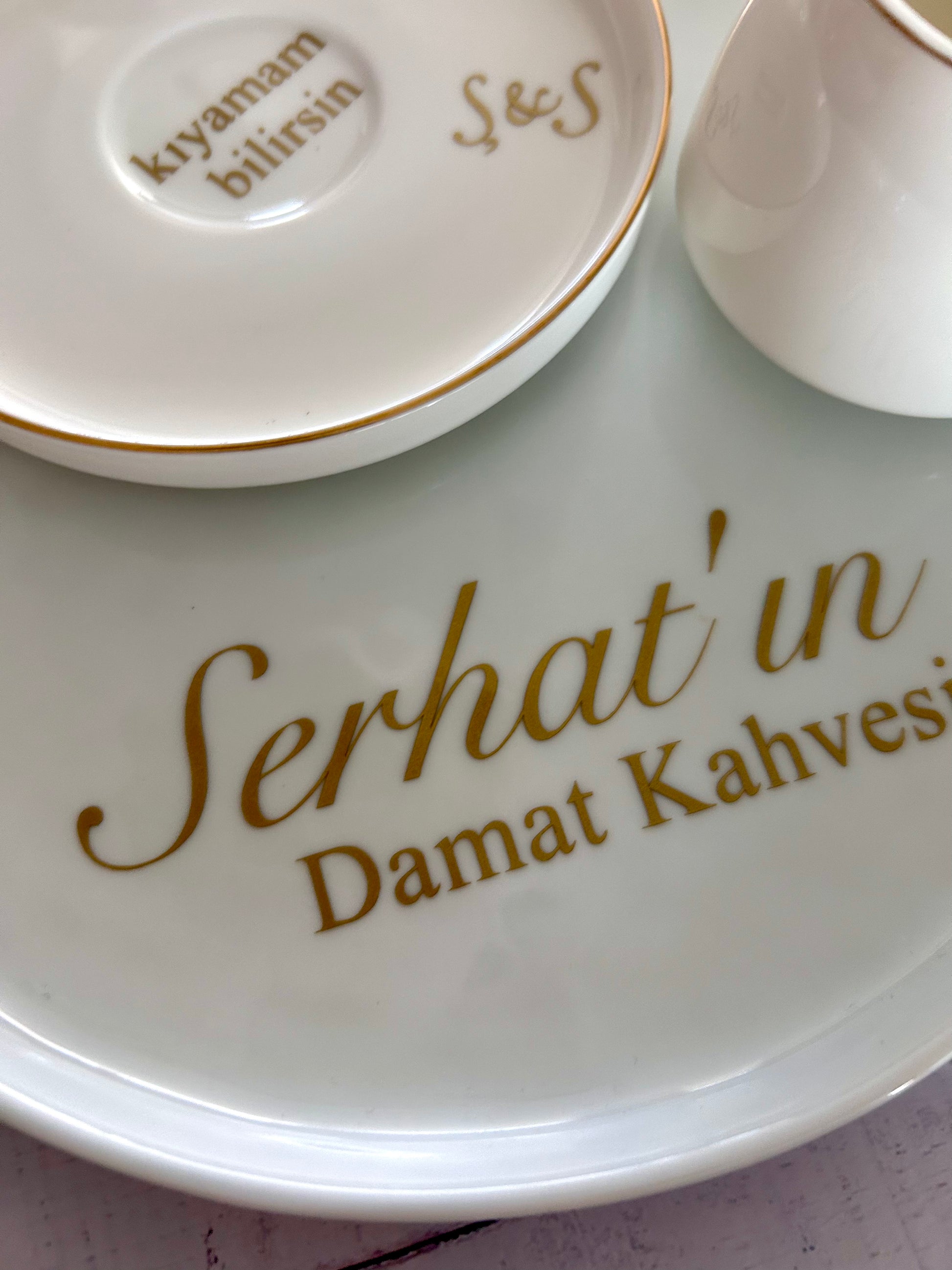 White ceramic plate with gold text 'Serhat'in Damat Kahvesi' and a small dish in the background.