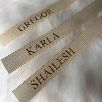 Three cream name tags with engraved names on a white fur background